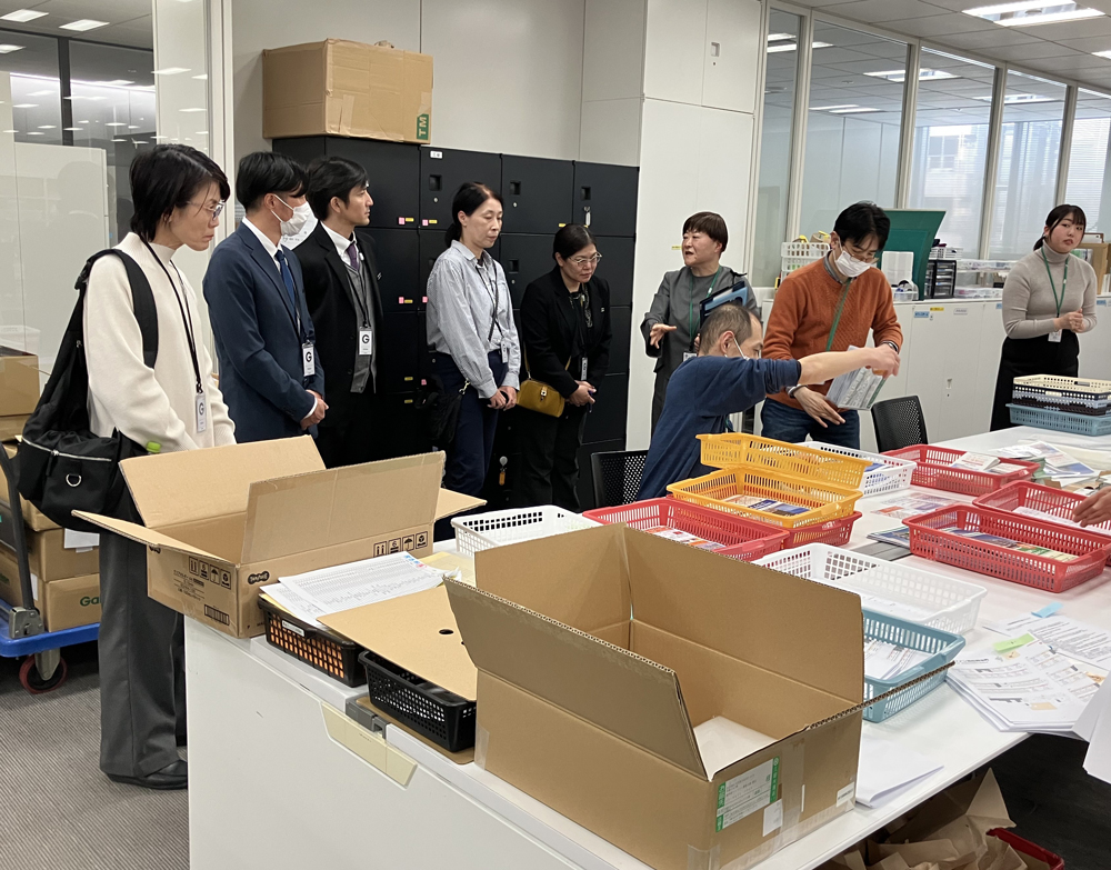 宣材の封入作業を視察する沖縄県立特別支援学校の先生方。