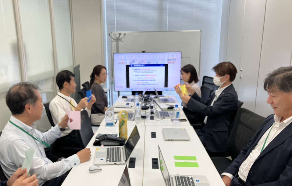 講師の指示で講座参加の社員たちが折り紙を切り、完成した形の違いに驚いています。